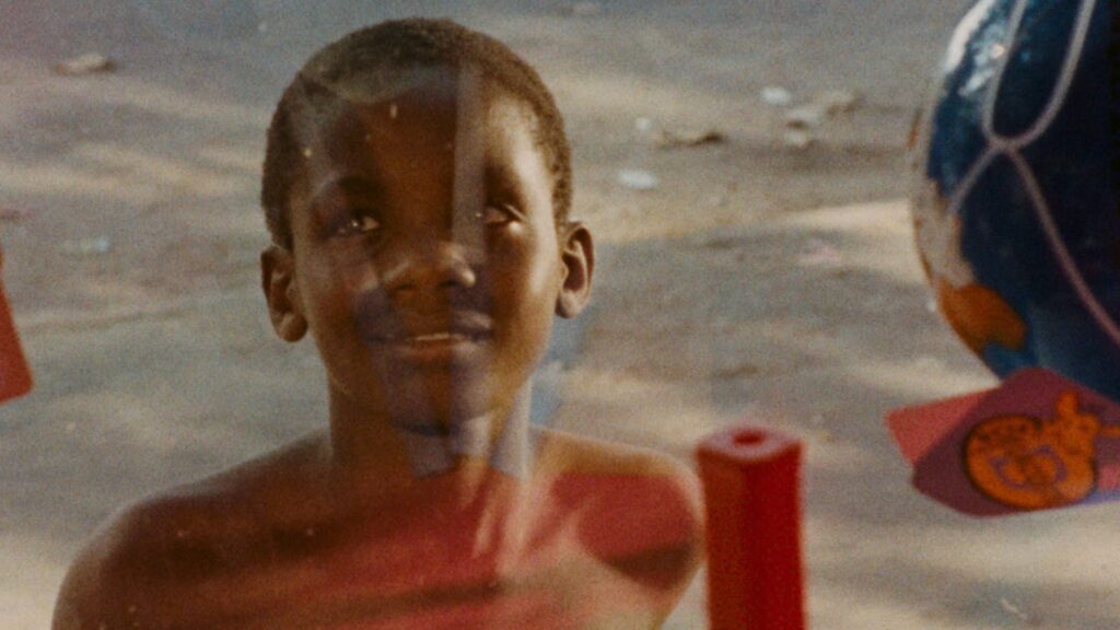 foto colorida de menino negro olhando através de vidro que reflete algumas letras em seu rosto