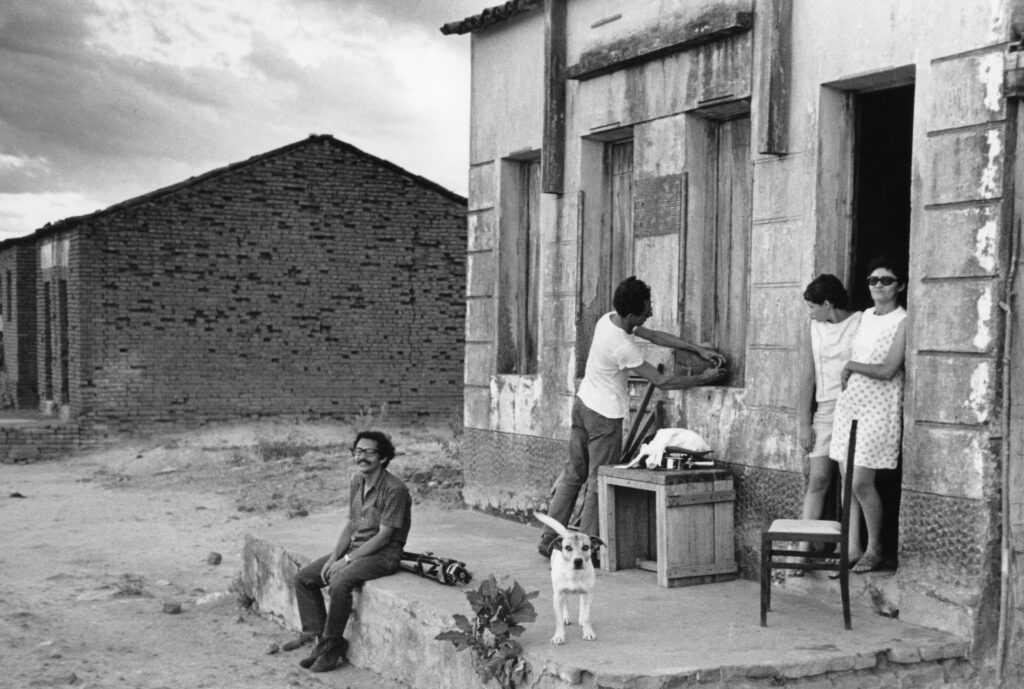 Foto preto e branco de três pessoas perto de uma casa