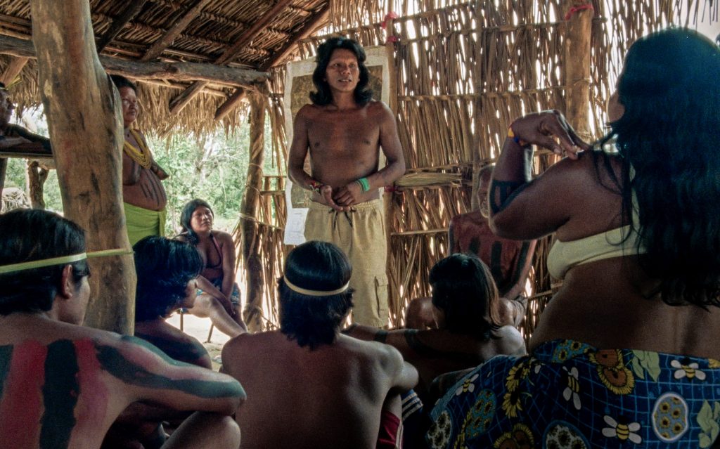 Grupo de indígenas conversando dentro de uma cabana de palha